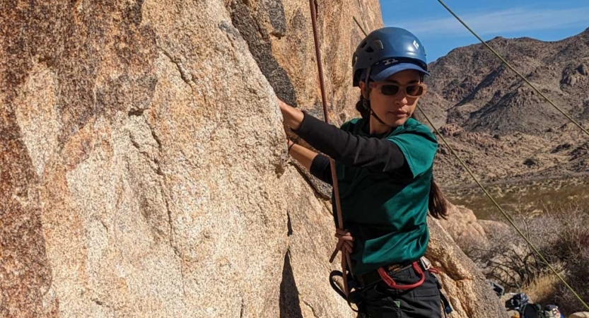 A person wearing safety gear is secured by ropes as they climb a rock wall. 